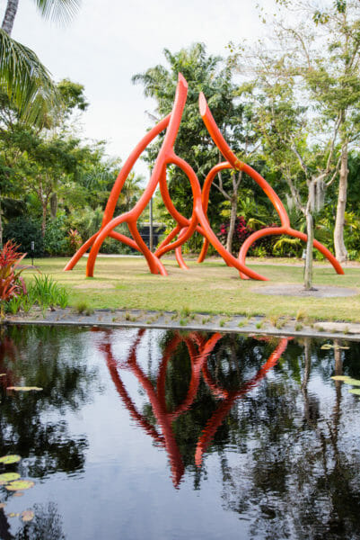 Large orange modern sculpture with reflection in water at Naples Botanical Gardens
