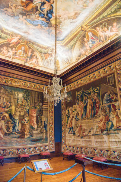 Large tapestries and a painted ceiling in a room in Hampton Court