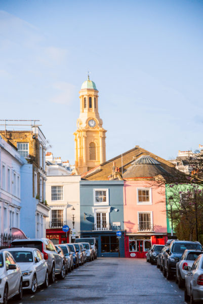 Yellow church tower behind pink and blue buildings in Notting Hill
